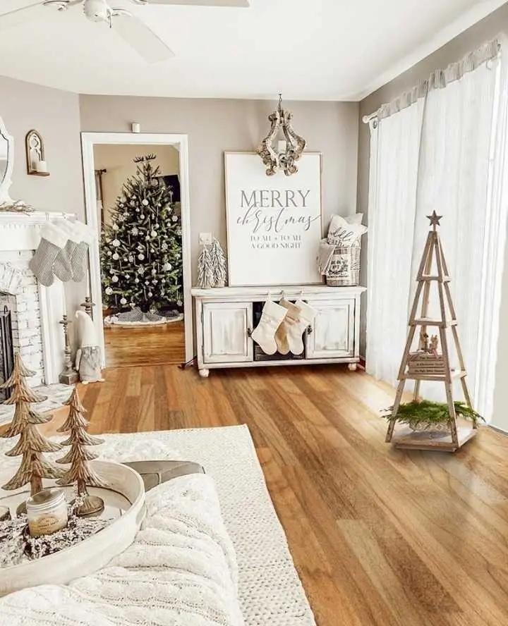 A living room decorated for Christmas with a tree, stockings, and holiday décor in neutral tones, including a "Merry Christmas" sign and wooden decorative trees.