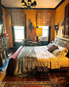 Boho maximalist bedroom with layered patterned bedding, warm mustard walls, eclectic decor, global-inspired textiles, and richly detailed accents creating a bold, cozy space.