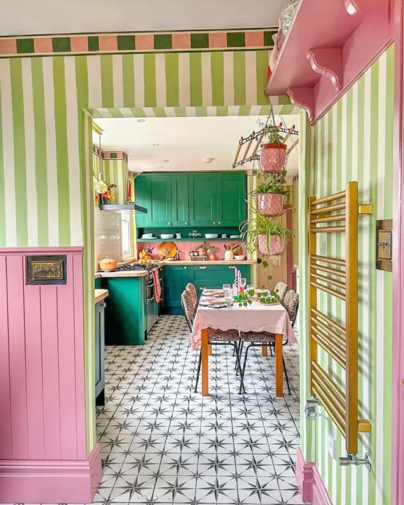 A funky kitchen and dining area with green and white striped walls, pink paneling, green cabinets, a patterned tile floor, and a table set for a meal.