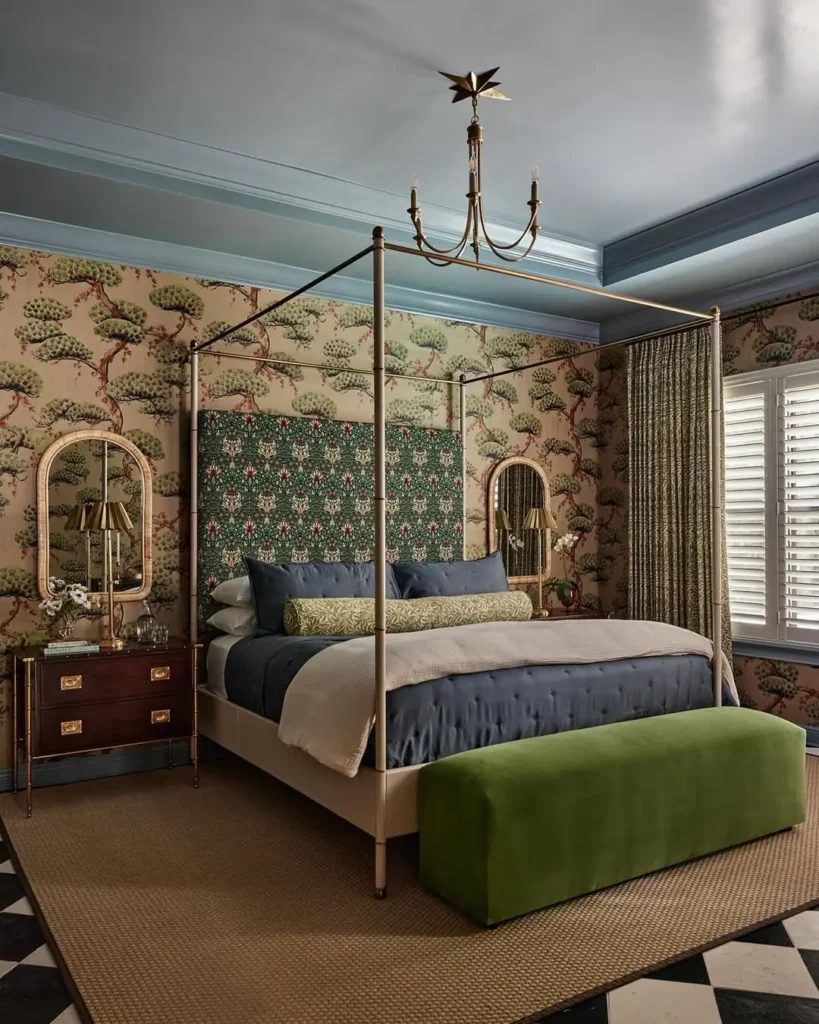 Eclectic bedroom with a four-poster bed, bold patterned wallpaper, mixed textures, blue bedding, green bench, statement chandelier, and layered vintage-inspired decor.