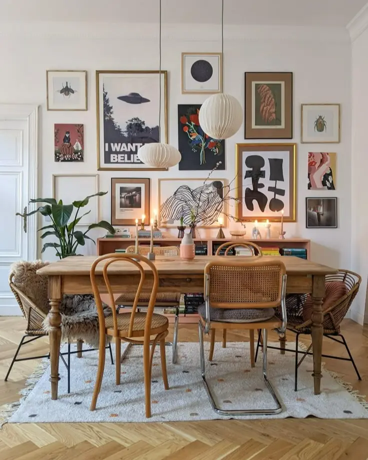 Eclectic dining room with mismatched chairs, wooden table, large gallery wall of mixed artwork, modern pendant lights, and layered textures creating a curated, artistic look.