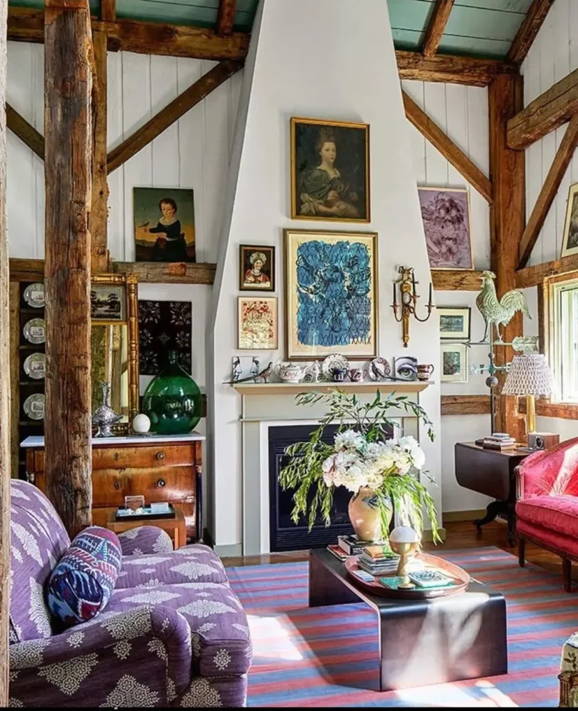 Eclectic living room with exposed wooden beams, eclectic patterned furniture, a central fireplace, framed artwork, decorative objects, and a coffee table with a flower arrangement.