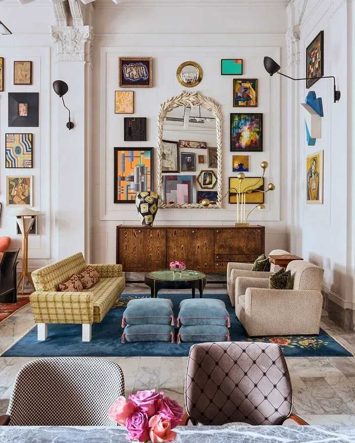 Colorful eclectic living room with mixed furniture styles, bold gallery wall art, patterned sofa, blue area rug, and layered textures creating a curated, artistic space.