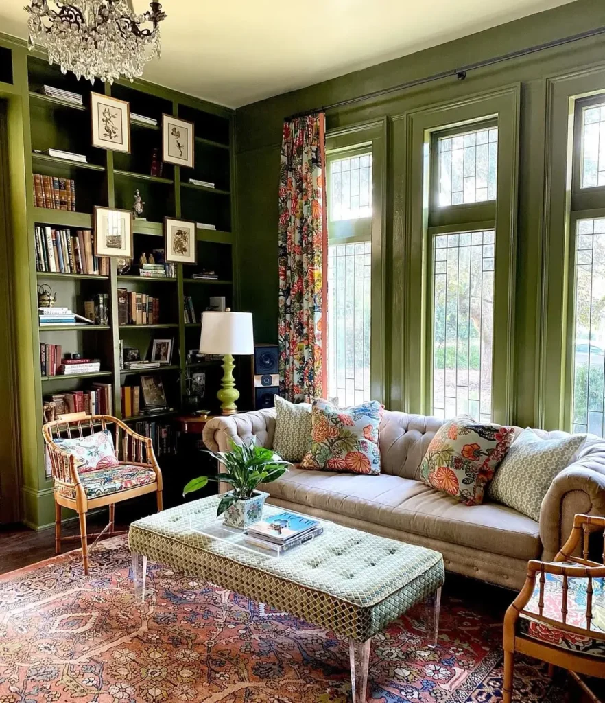 Eclectic living room with olive green built-ins, tufted sofa, patterned pillows, floral curtains, rattan chairs, and a colorful vintage rug creating a vibrant, curated space.