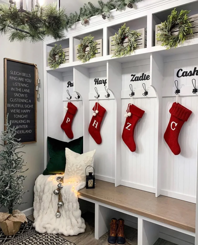 Festive Christmas mudroom featuring built-in cubbies and bench seating with smart storage solutions, decorated with red stockings, mini wreaths, evergreen garlands, cozy pillows, and holiday accents for an organized seasonal entryway.