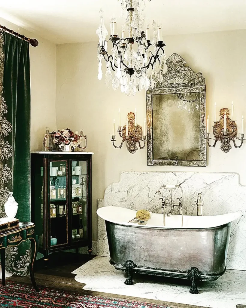 Elegant French country bathroom with a vintage clawfoot bathtub, ornate mirror, crystal chandelier, wall sconces, glass cabinet, and patterned curtains on the left.