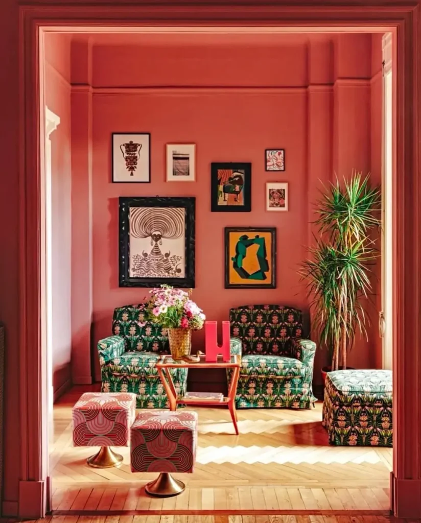 A colorful maximalist living room with pink walls, patterned green furniture, a gallery wall of framed art with art pieces that are the correct size and proportion for the room, a potted plant, and a wooden coffee table styled with flowers in a vase.