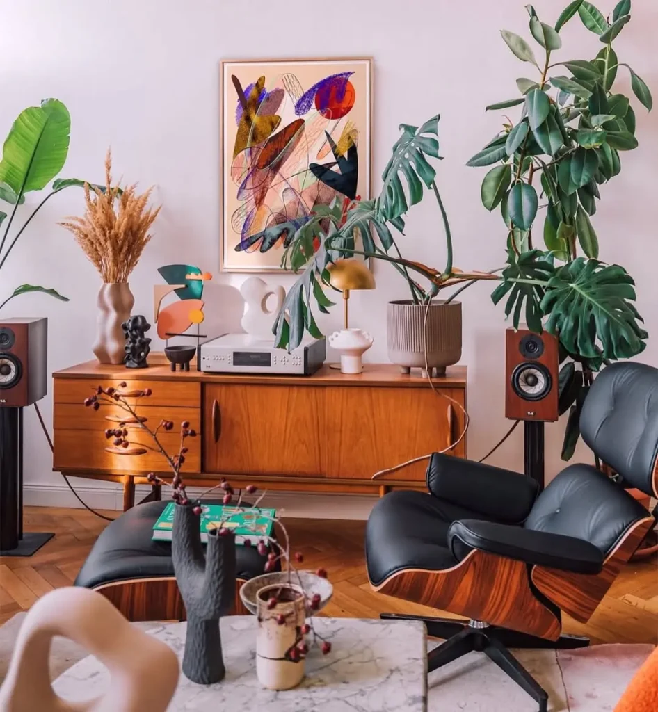 Mid-century modern living room featuring wooden furniture, a black lounge chair, large potted plants, abstract wall art, and decorative objects on a console table for a timeless mid century modern aesthetic.