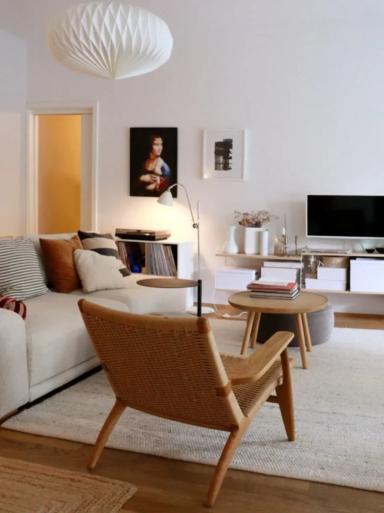 A modern living room with a beige sofa, woven chair, round coffee table, TV, wall art, books, and minimal decor on a light rug highlights mixing minimalist texture for a serene and sophisticated atmosphere.