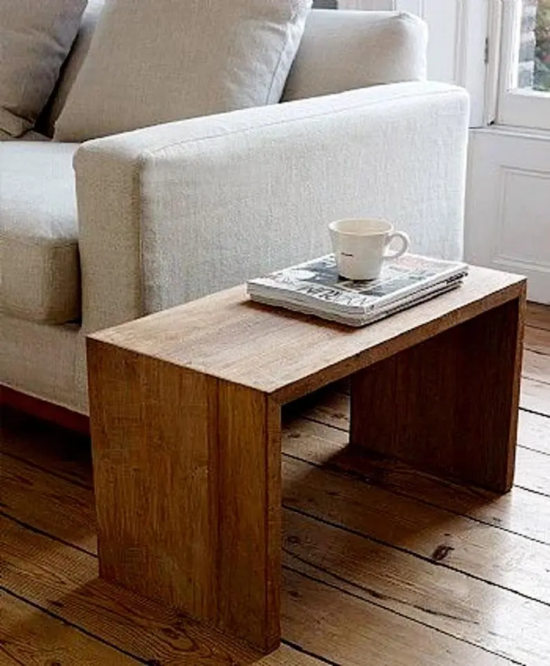 A small wooden side table with a magazine and a white mug on it, placed next to a light-colored sofa on a wooden floor.
