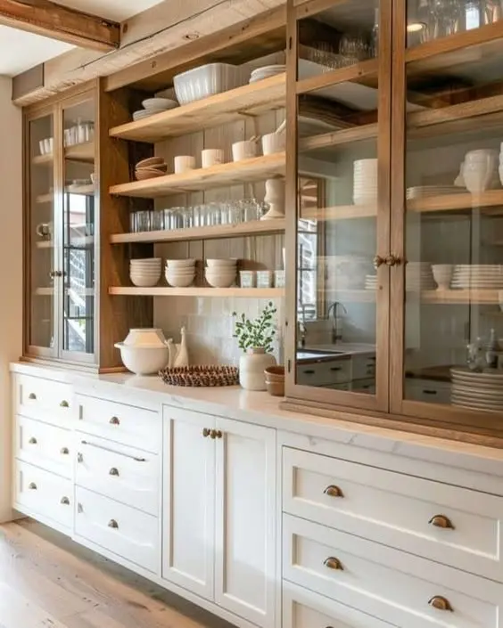A kitchen with white cabinets, glass-front wooden upper cupboards, and kitchen cabinet stackable shelves displaying neatly arranged white dishes and glassware.