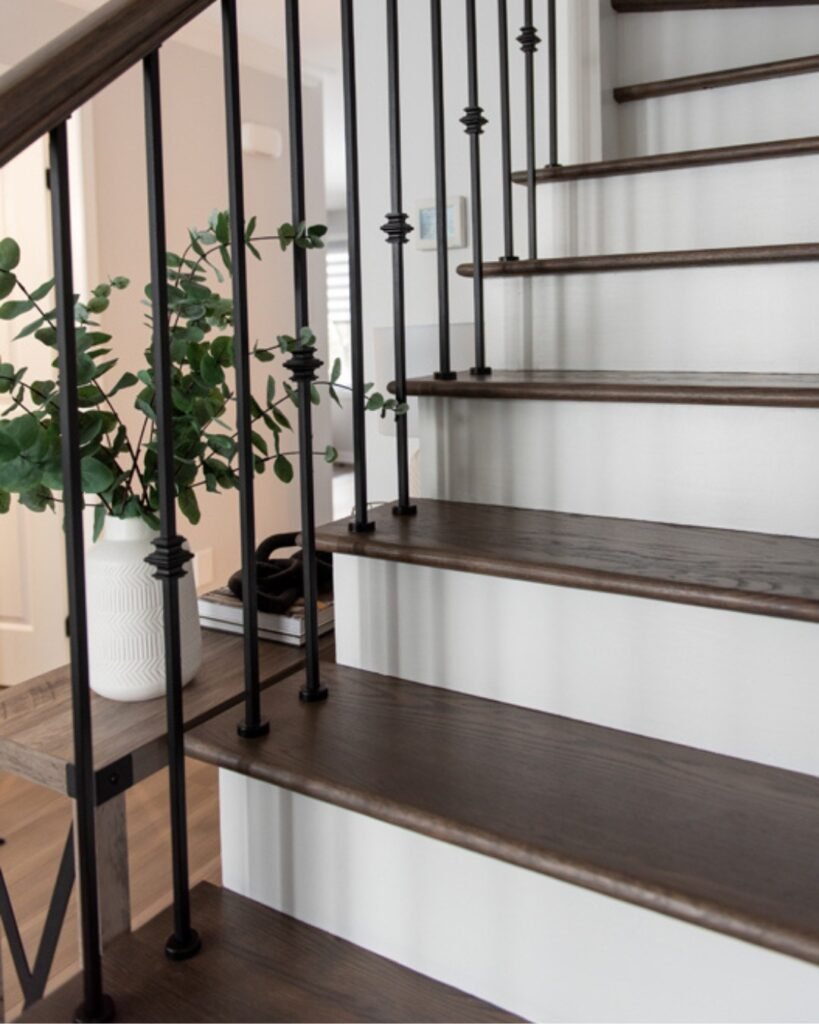A modern staircase with dark wooden steps and black metal railings, next to a white vase with green leafy branches on a small wooden table.