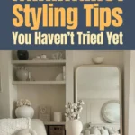 Minimalist living room with neutral decor, cozy textured blankets, a sculptural vase, shelves styled with simple objects, and a large mirror reflecting a serene, clutter-free space.