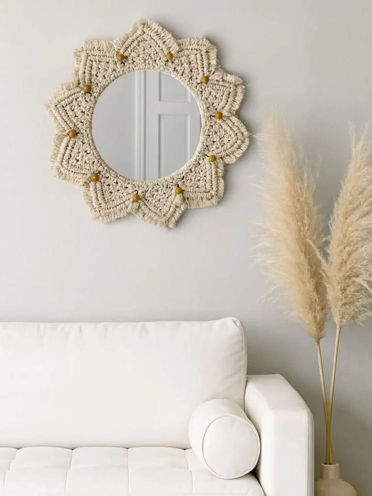 A round mirror with a beige woven frame adds a boho touch above a white couch; pampas grass in a vase stands to the right, enhancing the relaxed vibe.