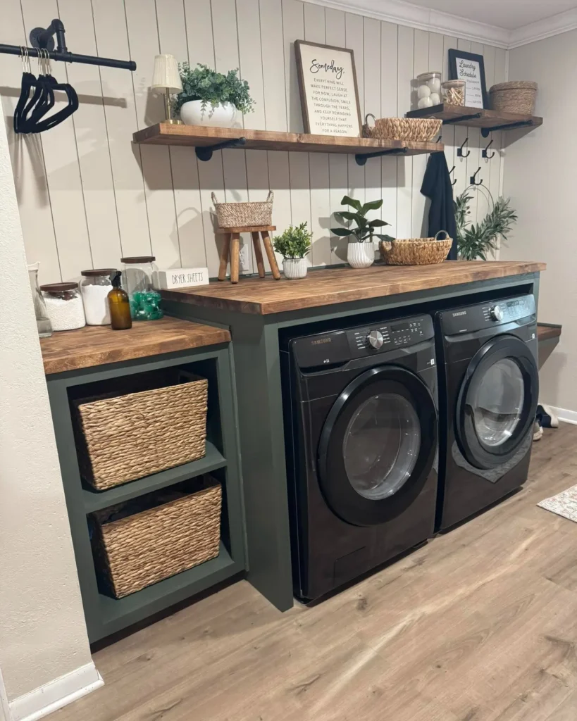 A laundry room with a black washer and dryer, wooden countertops and shelves, woven storage baskets, plants, jars, and a wall-mounted rod with hangers on a paneled wall.