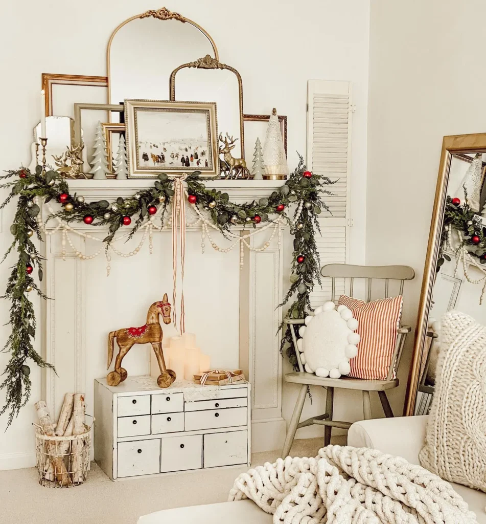 A decorated mantel with garland, framed art, candles, and ornaments sets a vintage farmhouse tone, featuring a wooden horse, a small chest of drawers, and a chair with pillows in a cozy living room.