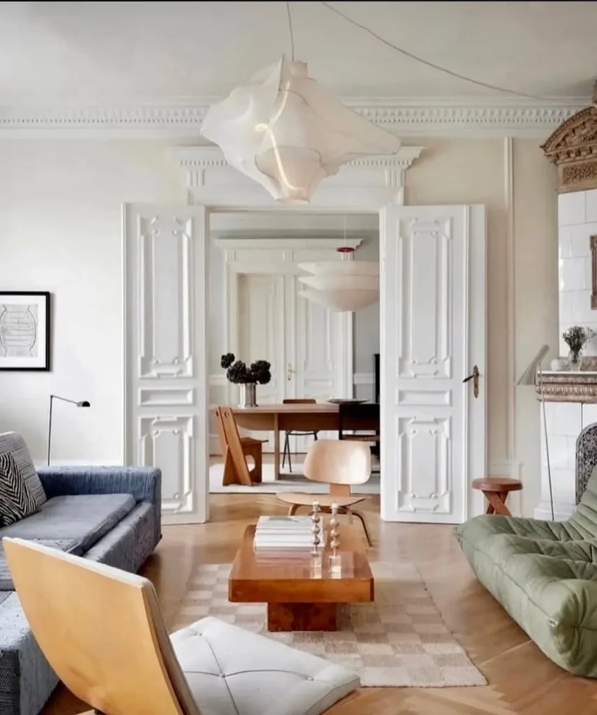Transitional mid-century modern living room with sculptural sofas, wood coffee table, minimalist lighting, classic white paneled doors, and warm wood flooring creating an elegant, airy space.