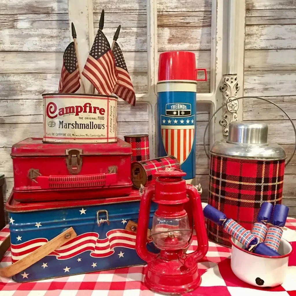 Vintage Fourth of July decor vignette featuring American flags, red lanterns, antique tins, a patriotic thermos, and rustic farmhouse accents.