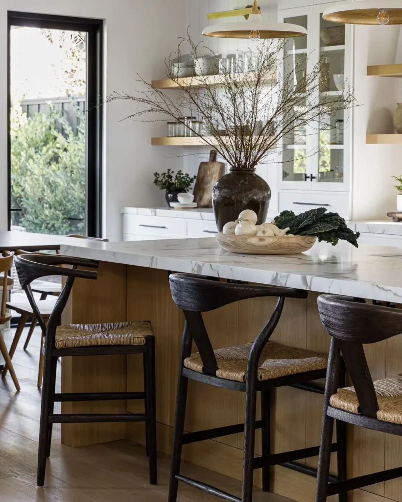 Organic modern kitchen with wood island, marble countertop, black wishbone stools, and oversized vase centerpiece.