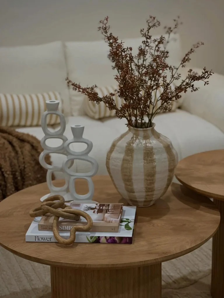 Modern coffee table styling with ceramic vase, sculptural candle holders, stacked books, and decorative chain accents.