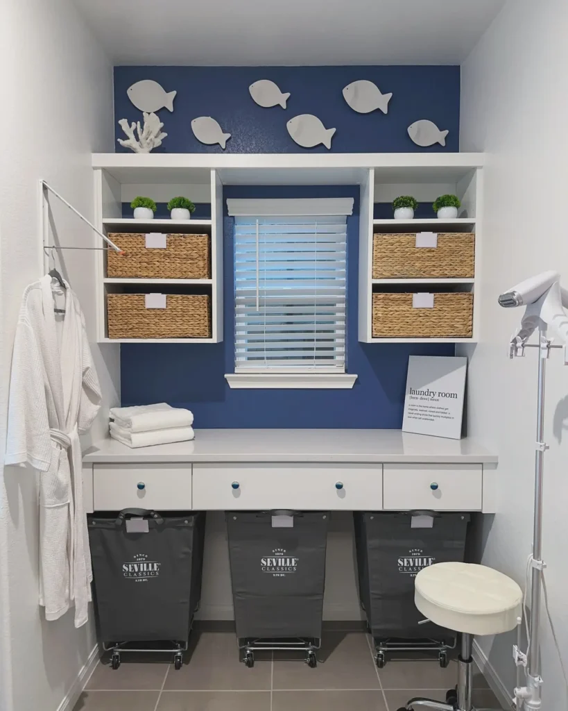 Custom laundry folding station with built-in white cabinetry, woven storage baskets, navy accent wall, rolling laundry hampers, wall hooks, and a space-saving organized laundry room design.
