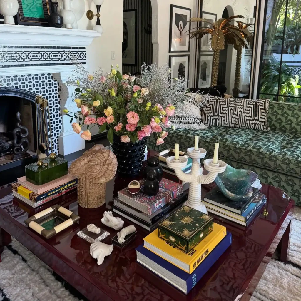 Eclectic coffee table decor with stacked books, sculptural objects, floral arrangement, and layered vintage accents.