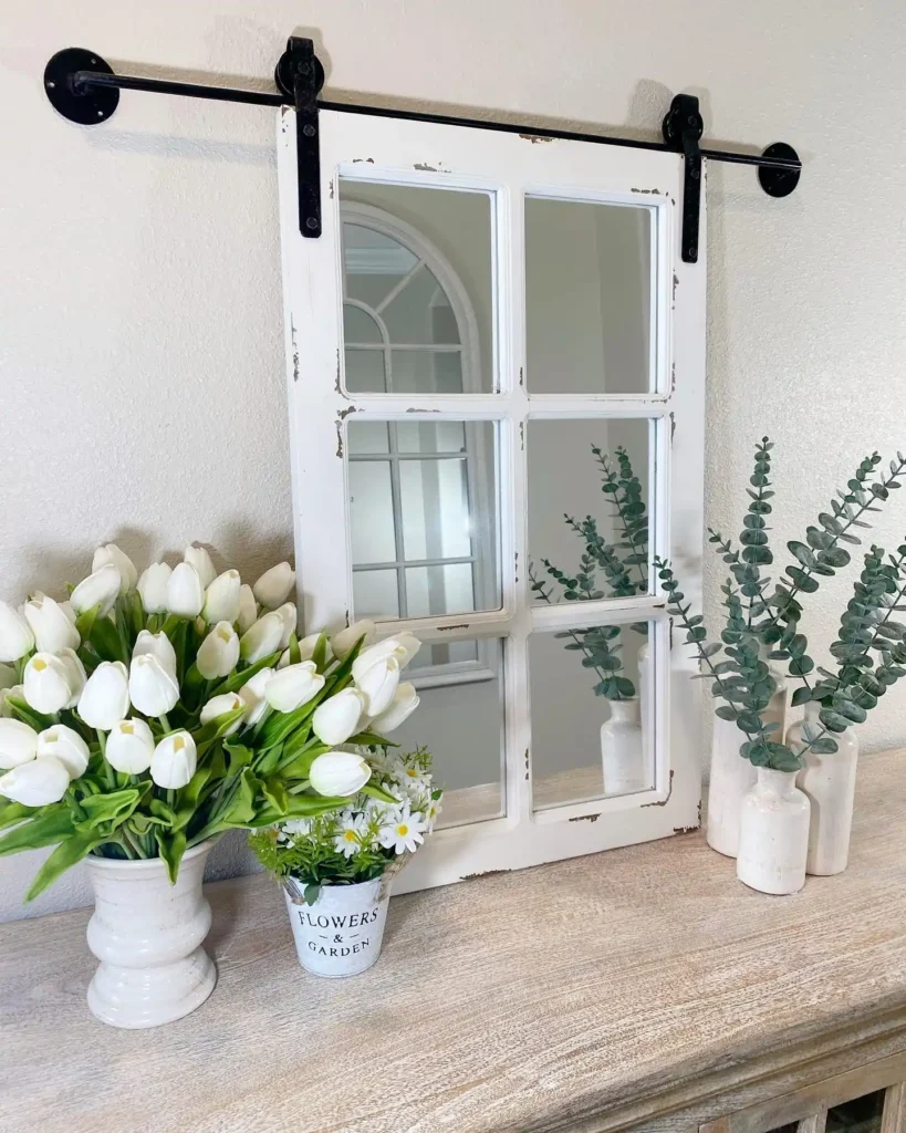Farmhouse barn door mirror with a distressed white frame styled on a console table with tulips and eucalyptus.