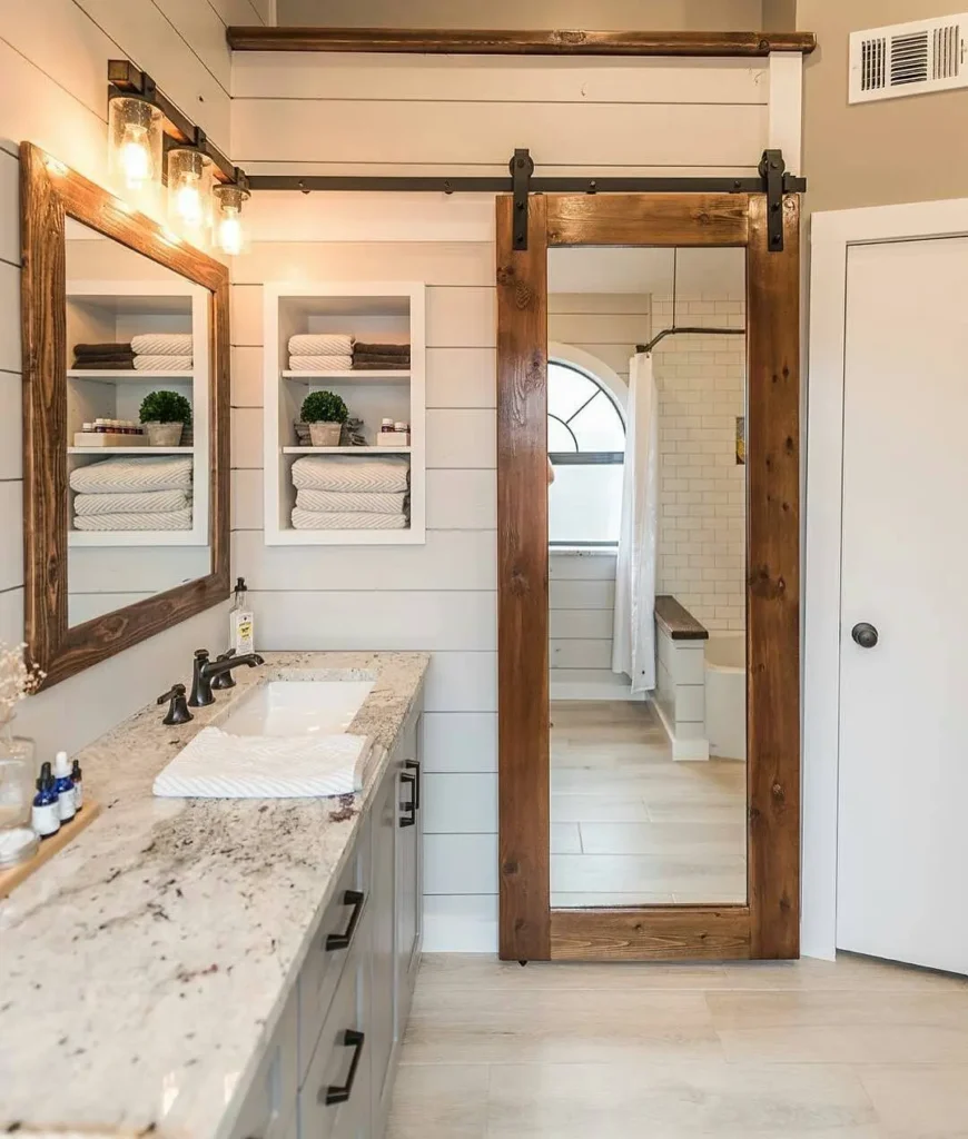 Rustic farmhouse bathroom featuring a barn door style mirror, shiplap walls, granite vanity, and open shelving.