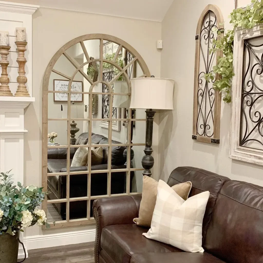 Farmhouse living room with an arched windowpane mirror, brown leather sofa, and neutral rustic decor.