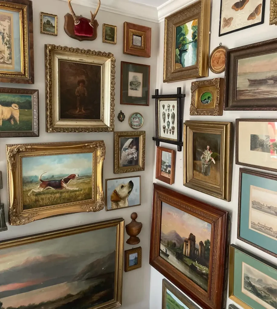 A corner gallery wall with vintage frames and art, densely decorated with framed paintings, drawings, and prints, including landscapes, animals, buildings, and botanical illustrations.