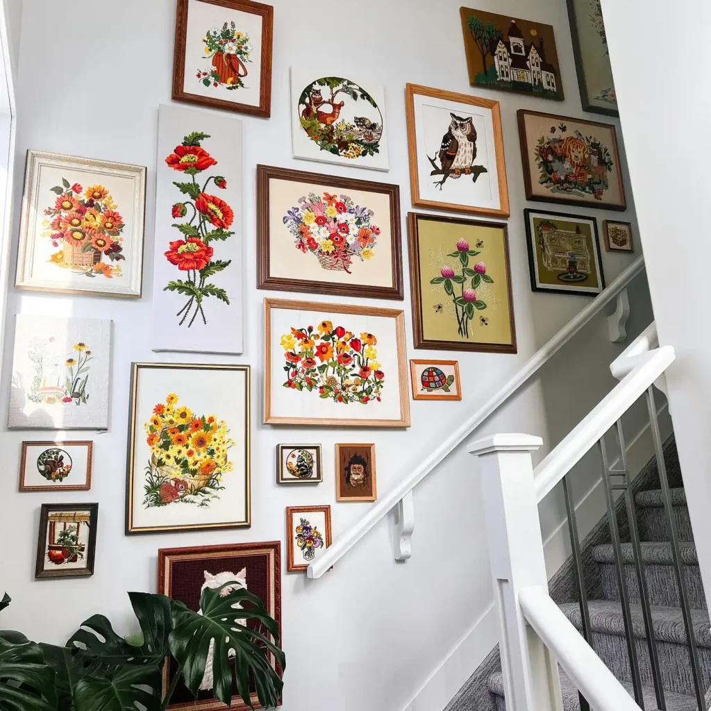 A staircase wall becomes a gallery wall with old and new framed floral and animal artworks in various sizes, complemented by a green potted plant at the bottom of the stairs.