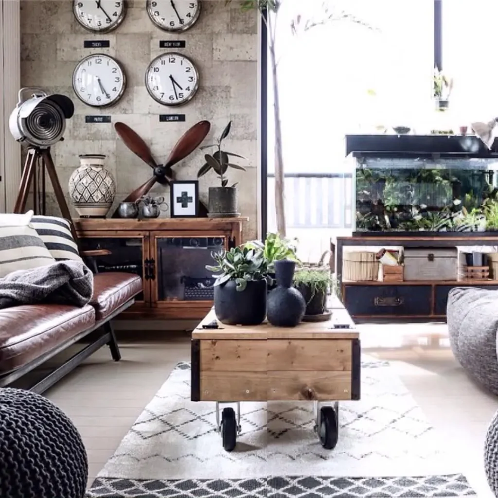 Industrial chic living room with a rustic wood coffee table on casters, leather sofa, vintage wall clocks, metal accents, indoor plants, and layered neutral textiles in a modern loft-style space.