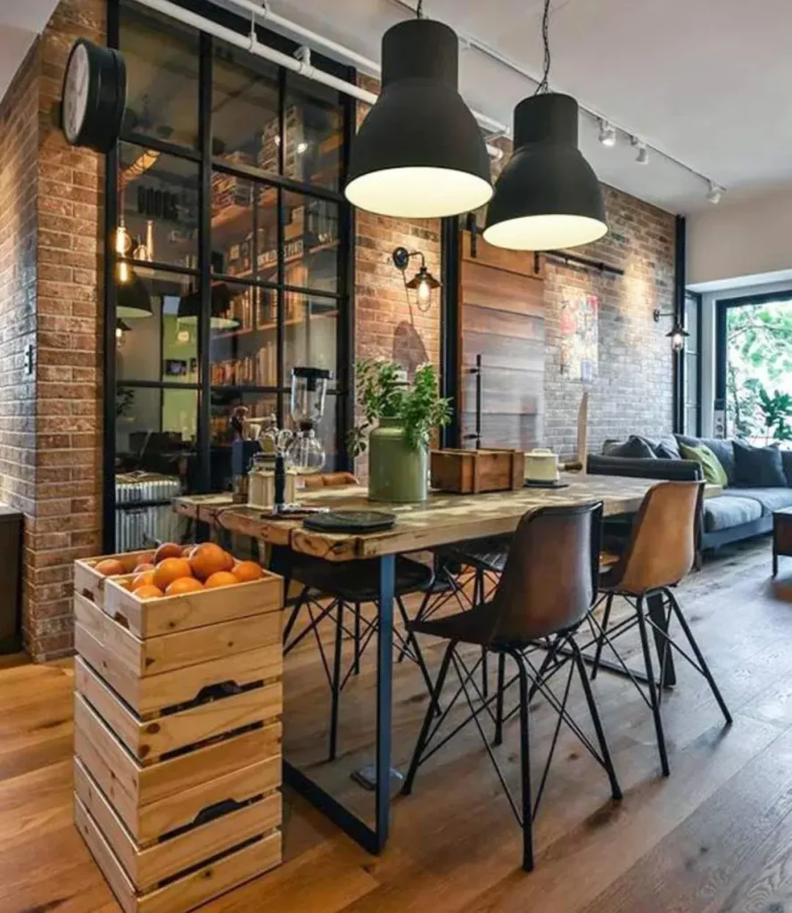 Industrial chic living space with exposed brick walls, black metal pendant lights, a rustic wood dining table, leather dining chairs, glass partitions, and warm wood flooring in a modern loft-style interior.