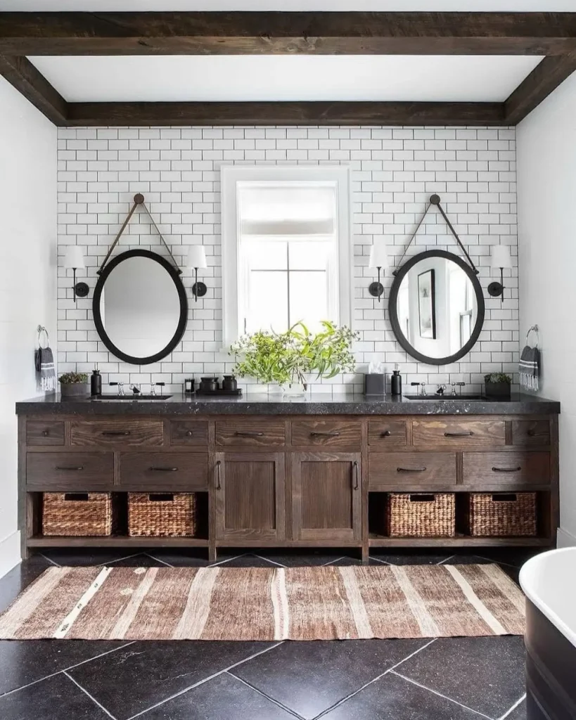 Industrial farmhouse bathroom with a dark wood double vanity, black countertop, round mirrors with leather straps, white subway tile backsplash, woven basket storage, and rustic modern bathroom decor.