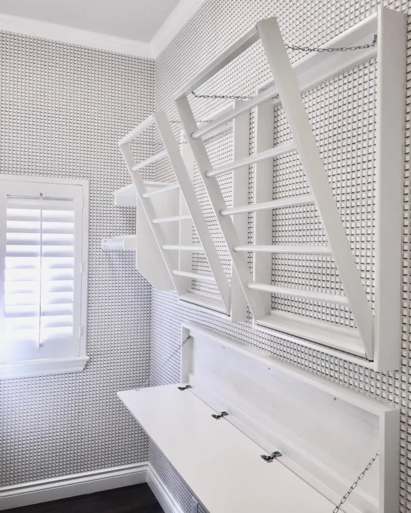 Wall-mounted laundry folding table with fold-down design and overhead drying racks, featuring a clean white finish and space-saving solution for a small, organized laundry room.