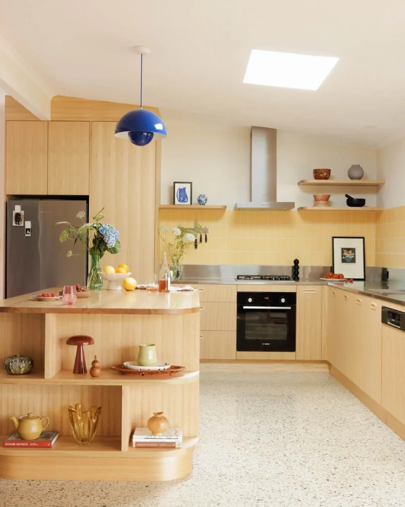 Mid-century modern kitchen with warm wood cabinetry, a curved island with open shelving, terrazzo flooring, and soft rounded edges throughout the space.