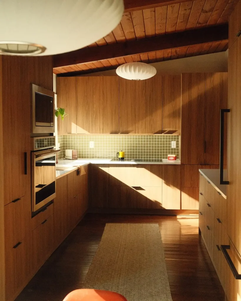 Mid-century modern kitchen with flat-front wood cabinetry, minimal black hardware, integrated pulls, and clean-lined design highlighted by warm natural light.