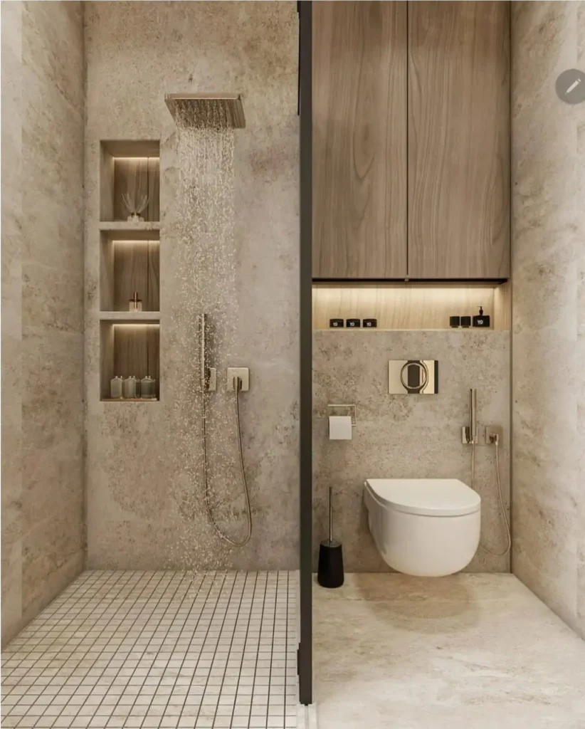 Organic modern bathroom with textured stone walls, walk-in rainfall shower, built-in shower niches, floating toilet, warm wood cabinetry, and soft ambient lighting for a minimalist spa-like design.