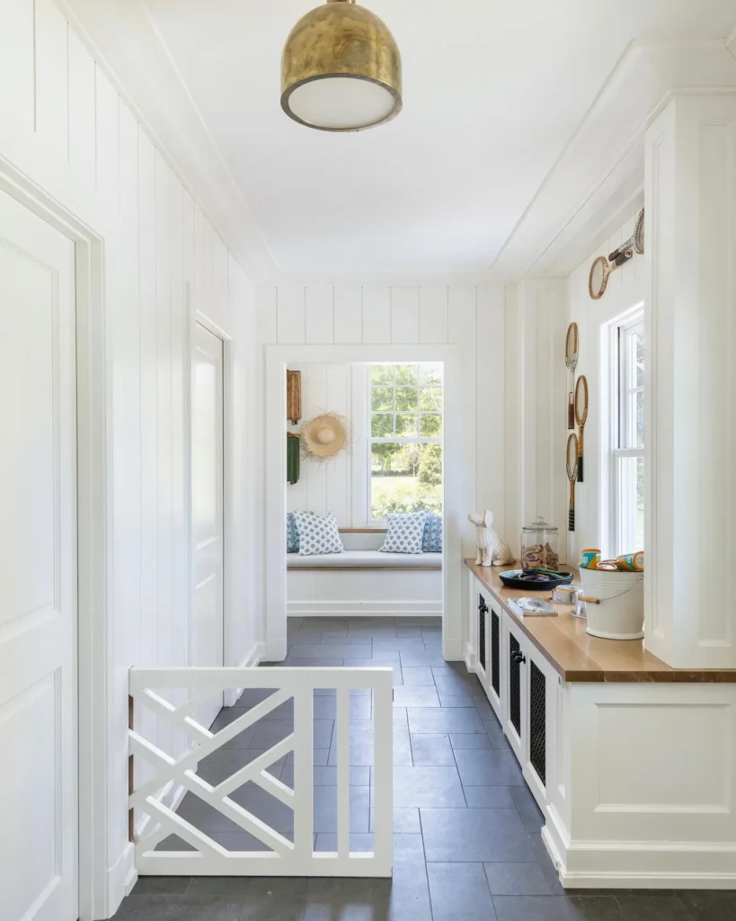 Pet-friendly mudroom with white shiplap walls, gray tile flooring, built-in storage cabinets, wood countertop, safety gate, and a cozy window bench designed for an organized, family-friendly entryway.