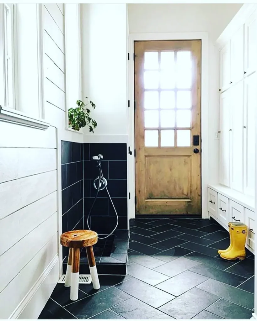 Pet-friendly mudroom with built-in dog wash station, black herringbone tile flooring, white shiplap walls, custom storage cabinets, and a rustic wood entry door designed for everyday function.