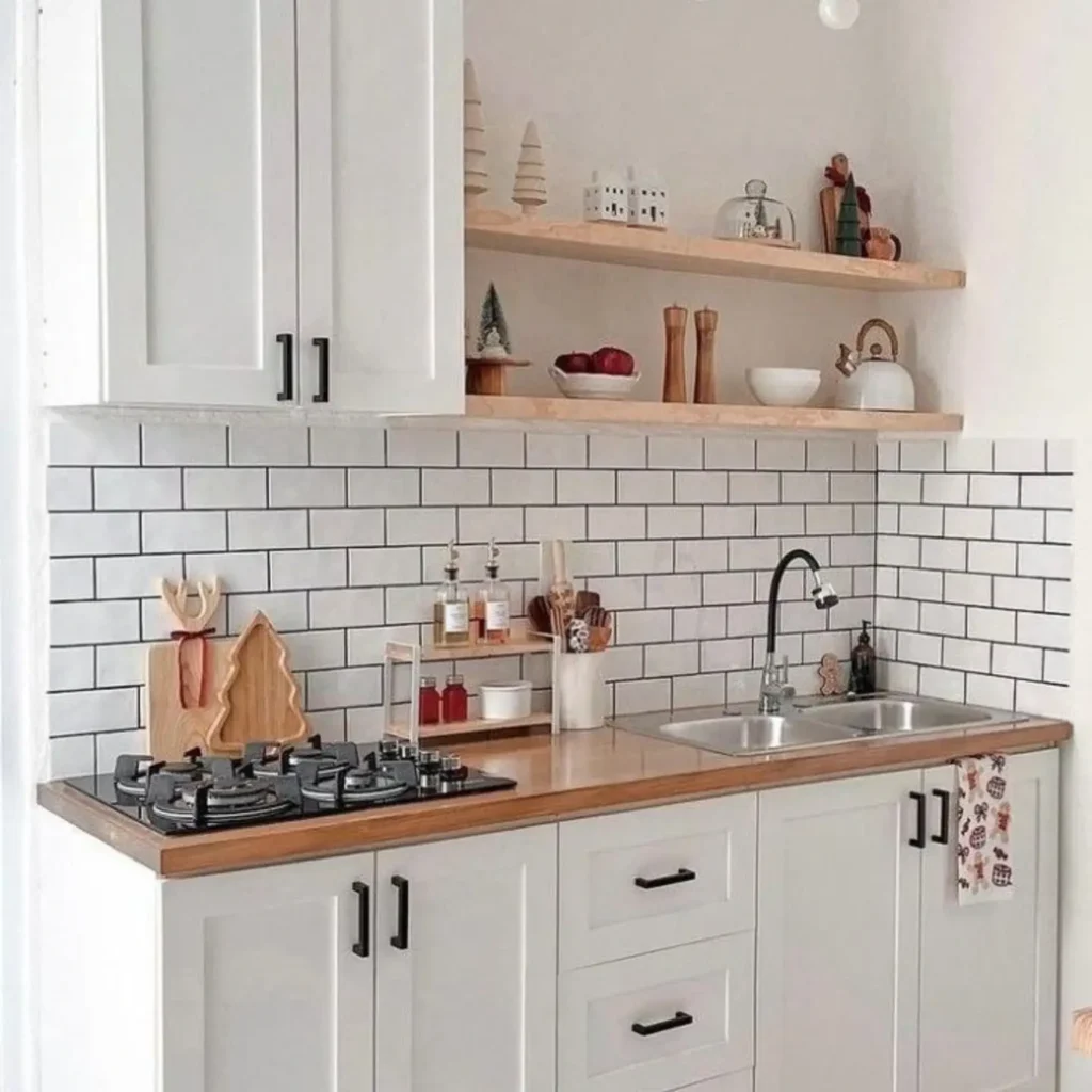 A modern kitchen with white cabinets, a wooden countertop, a gas stove, a sink, open shelves with decor, and subway tiles with colored grout for a contemporary backsplash.