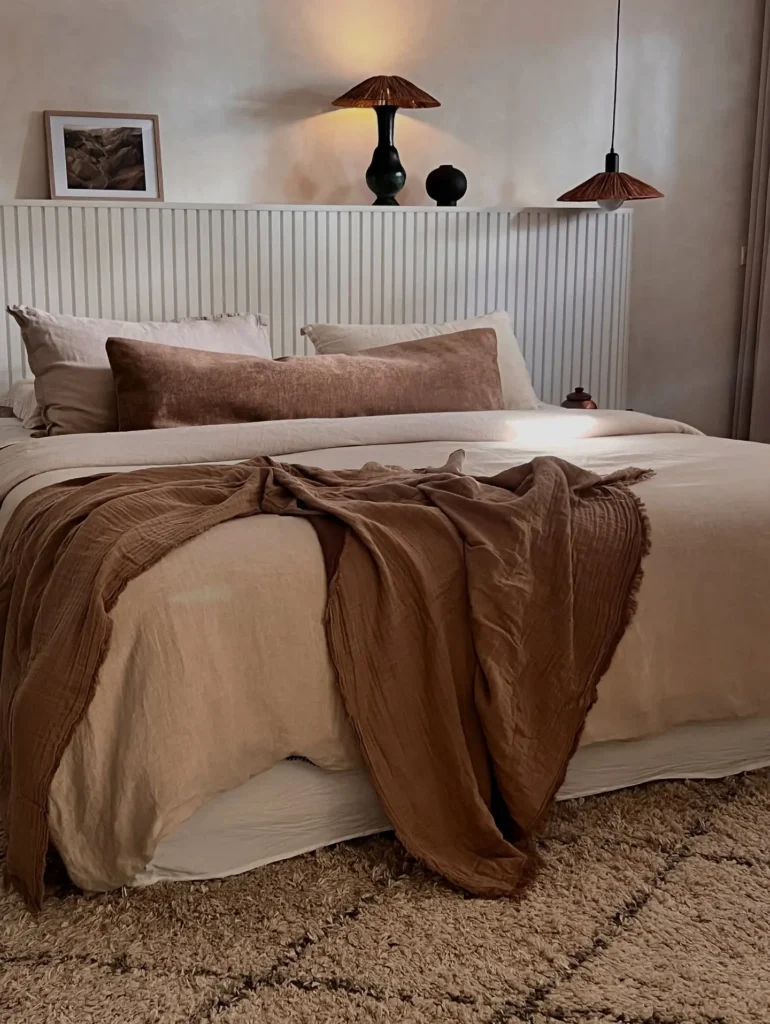 Wabi-sabi bedroom with layered neutral bedding, linen textures, asymmetrical throws, warm ambient lighting, and a calm, earthy, minimalist aesthetic.