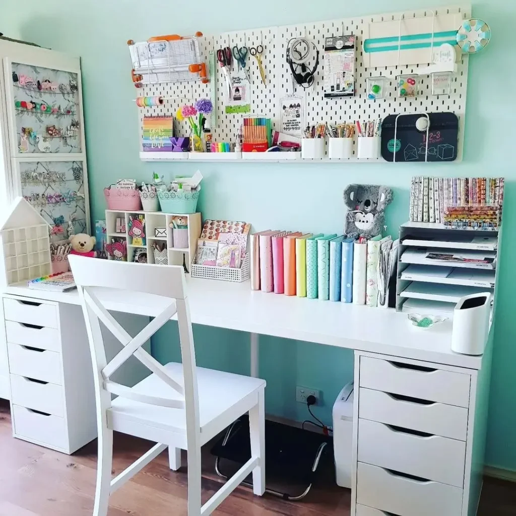 White wall pegboard in a pastel craft room with shelves holding stationery, scissors, planners, and colorful supplies above a desk.