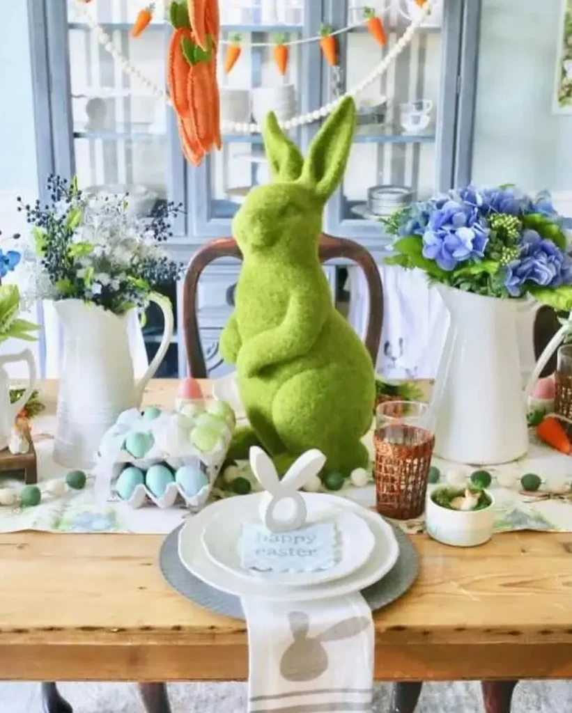 Easter table decor with green moss bunny centerpiece, pastel eggs, carrot garland, and spring floral arrangements.