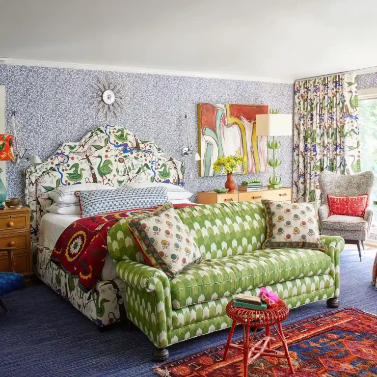Funky bedroom decor with bold patterned wallpaper, green ikat sofa, and colorful layered textiles.
