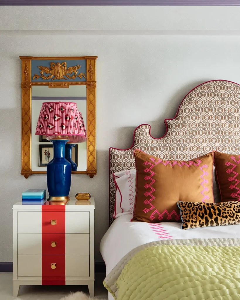 Funky bedroom decor with patterned upholstered headboard, bold accent pillows, and colorful nightstand with statement lamp.