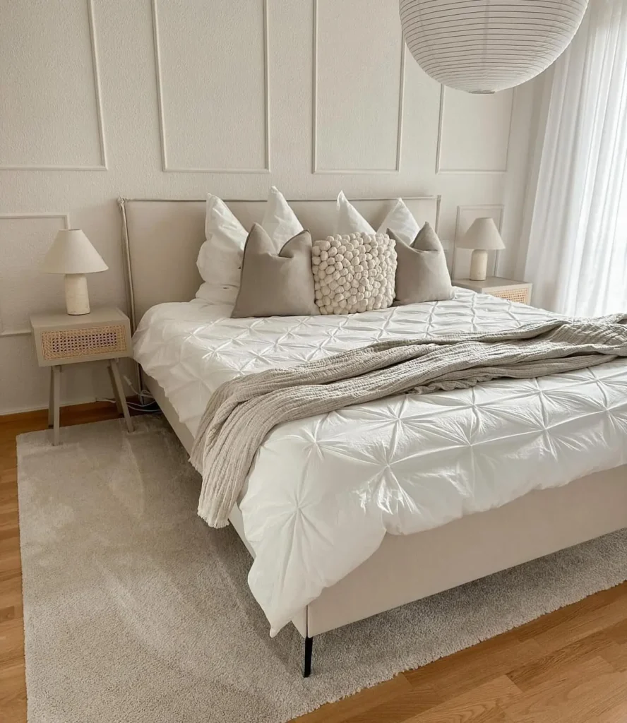 Modern minimalist bedroom featuring textured white duvet, neutral accent pillows, light wood nightstands, and soft area rug.