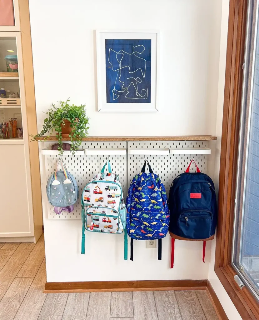 Small entryway wall pegboard with hooks holding kids’ backpacks, floating shelf, and framed artwork above.