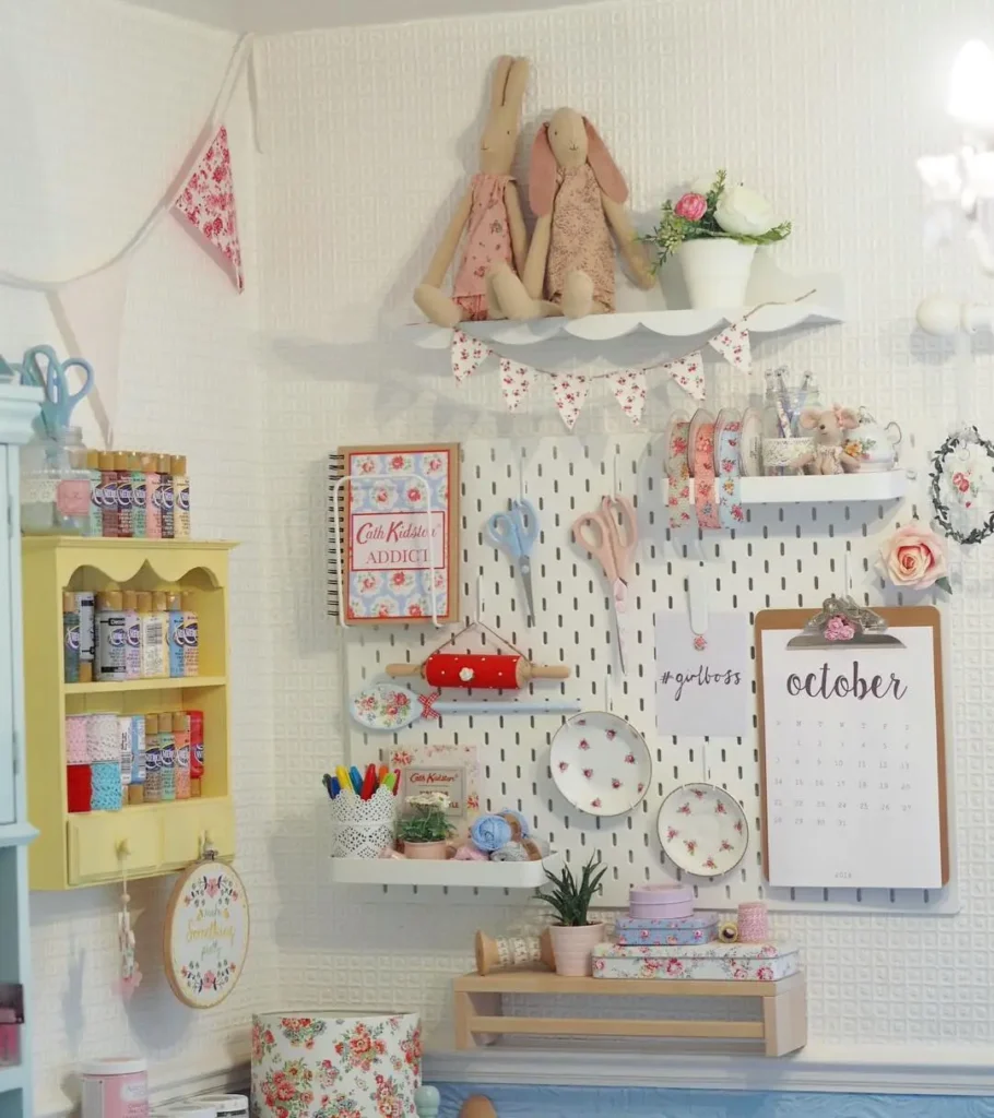 White wall pegboard in a cottage-style craft room with shelves holding scissors, floral decor, ribbons, and a monthly calendar.