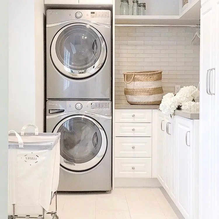 Small white laundry room with stackable washer and dryer, built-in cabinets, subway tile backsplash, and woven basket storage.